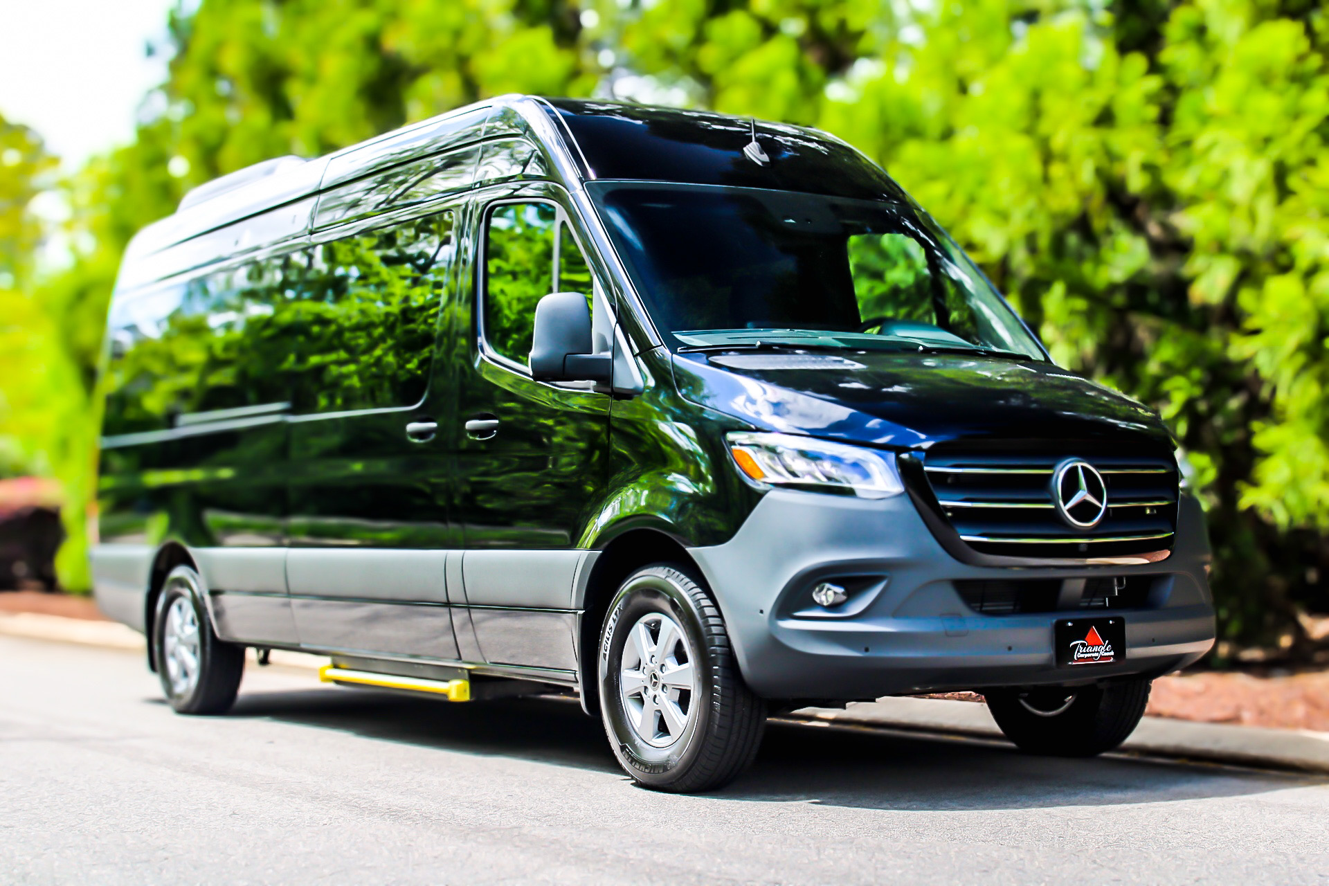Black Mercedes-Benz Sprinter luxury shuttle van parked on a tree-lined street